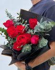 Person holding a bouquet of red roses and greenery against a light blue background