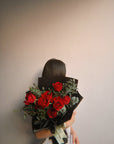 Person holding a bouquet of red roses against a plain background