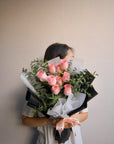 Person holding a bouquet of pink roses against a plain background