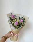 Bouquet of lilac tulips with green leaves held by a hand on a light background
