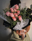 Bouquet of pink roses held by a person wearing a green outfit.