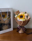 Bouquet of flowers wrapped in brown paper with a bow, placed on a white surface.