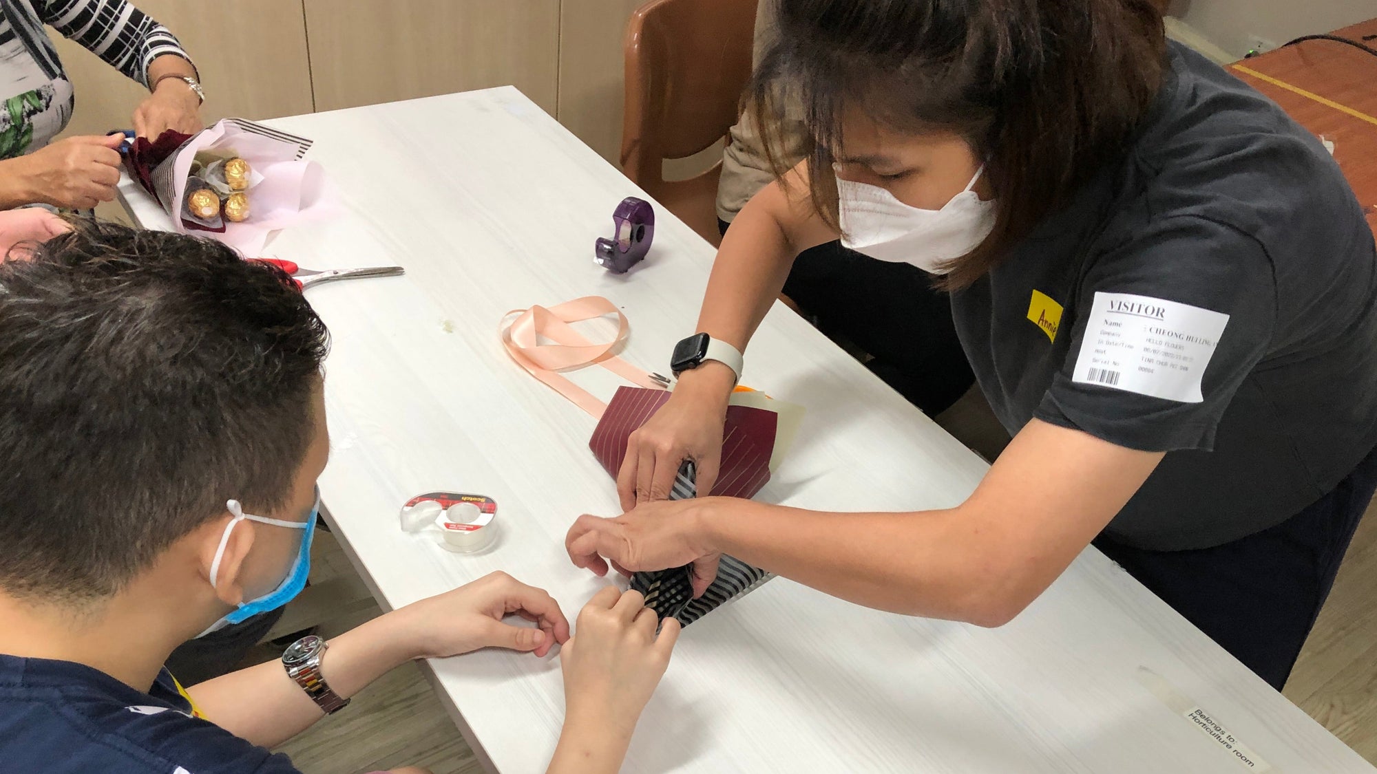 Person assisting a child with a craft activity at a table.