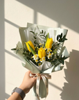 Bouquet of yellow tulips and greenery held by a hand against a light background