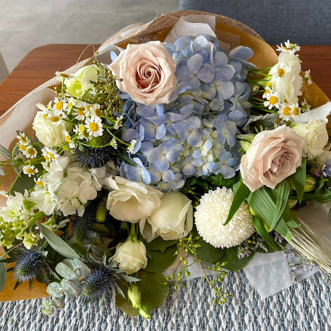 Fresh floral arrangement for corporate gifting with hydrangea, roses, and white pom pom blooms.