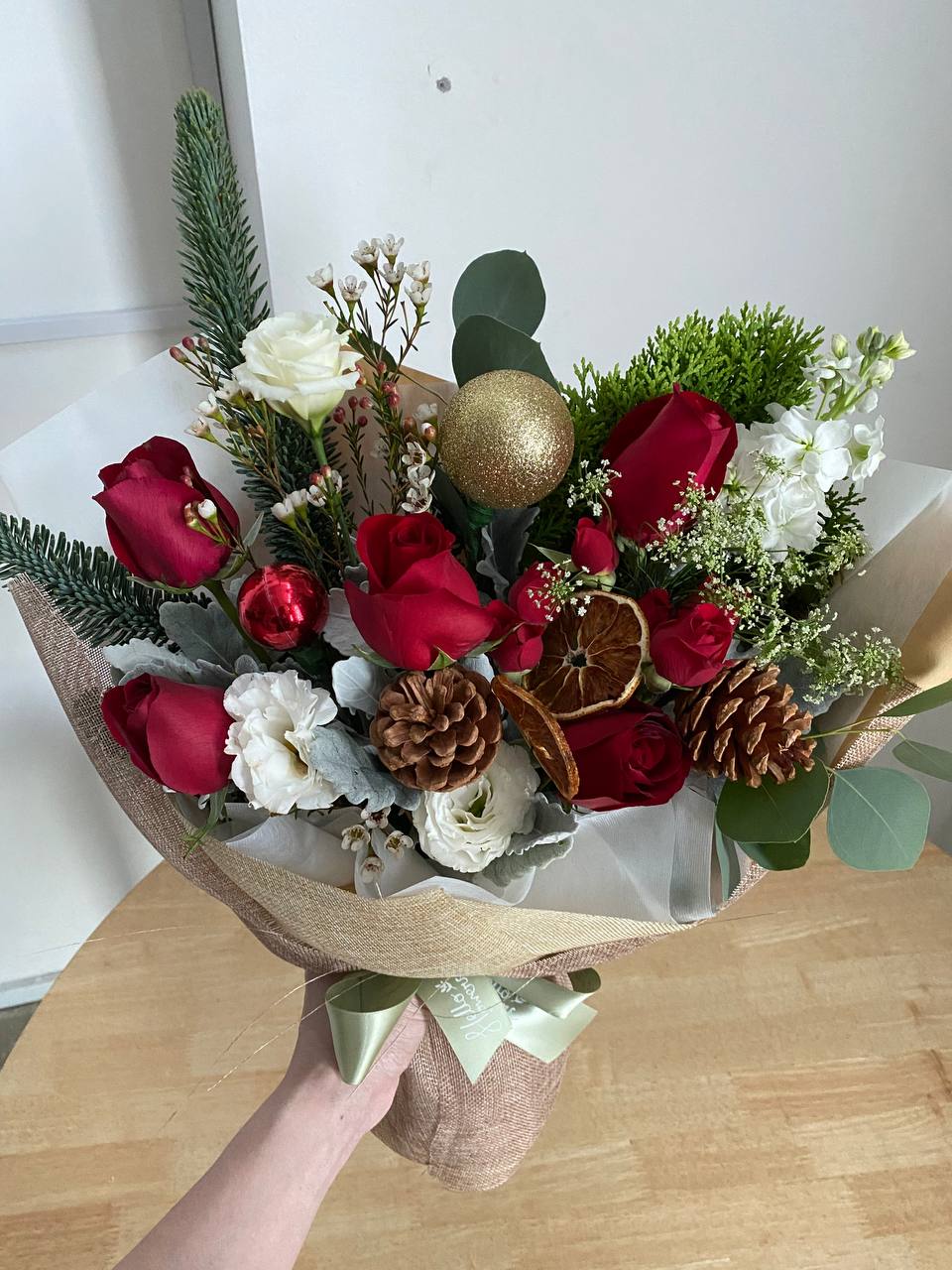 hand holding whimsical winter bouquet with red roses, white flower blooms, and sliced dried orange