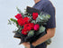 Person holding a bouquet of red roses and greenery against a light blue background