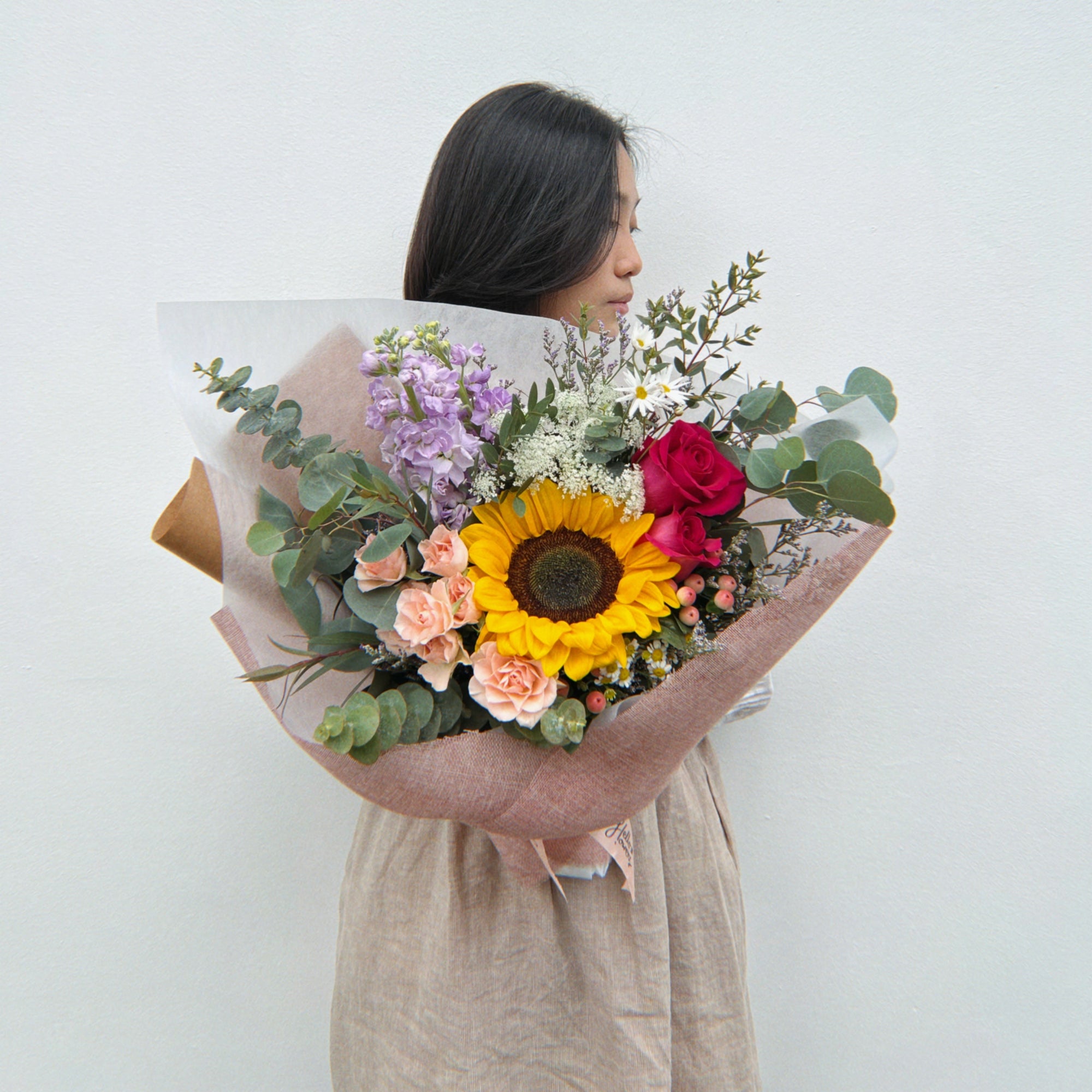 Person holding a bouquet of flowers with sunflower against a white background
