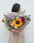 Person holding a bouquet of flowers with sunflower against a white background