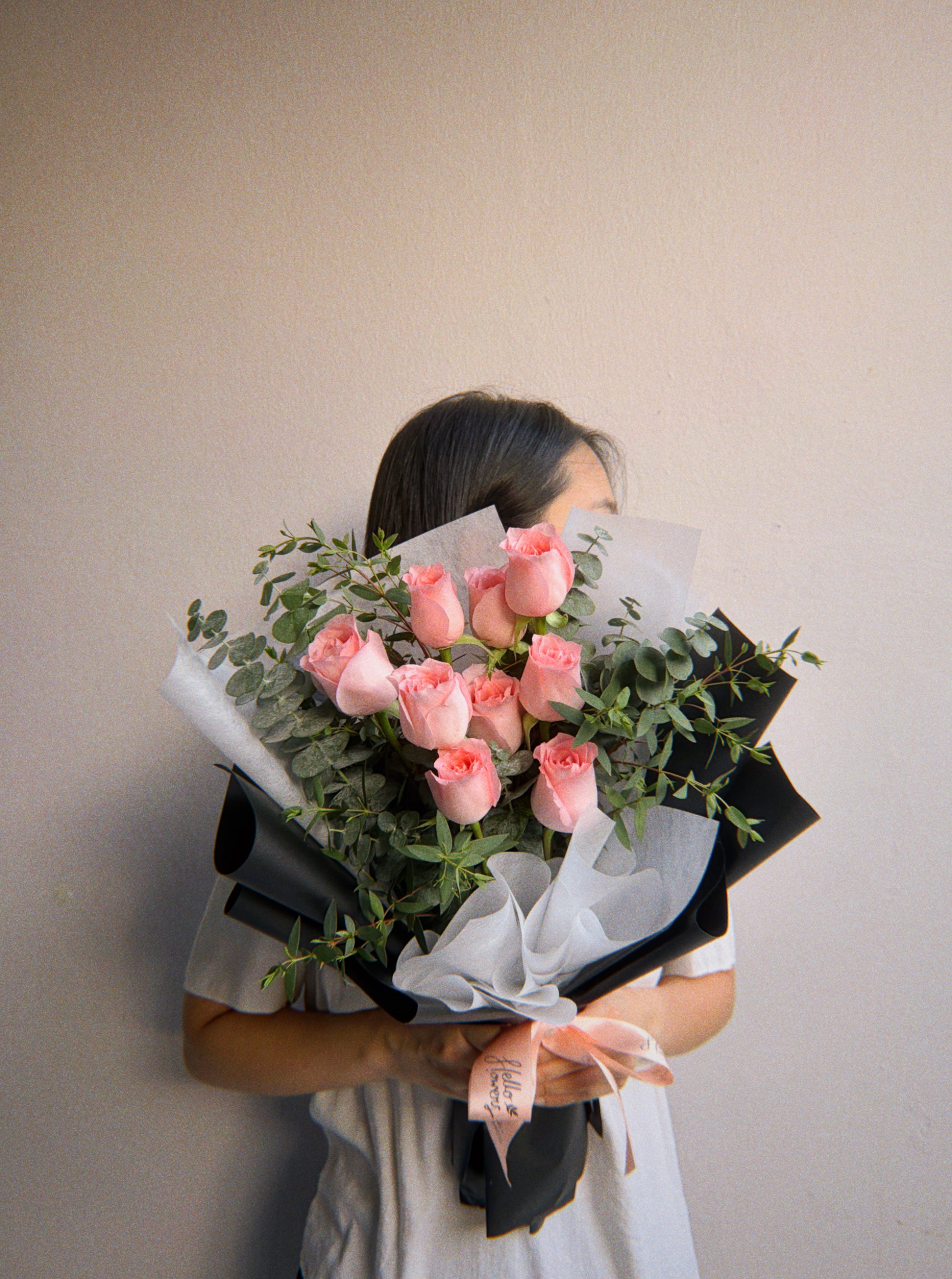 Person holding a bouquet of pink roses against a plain background