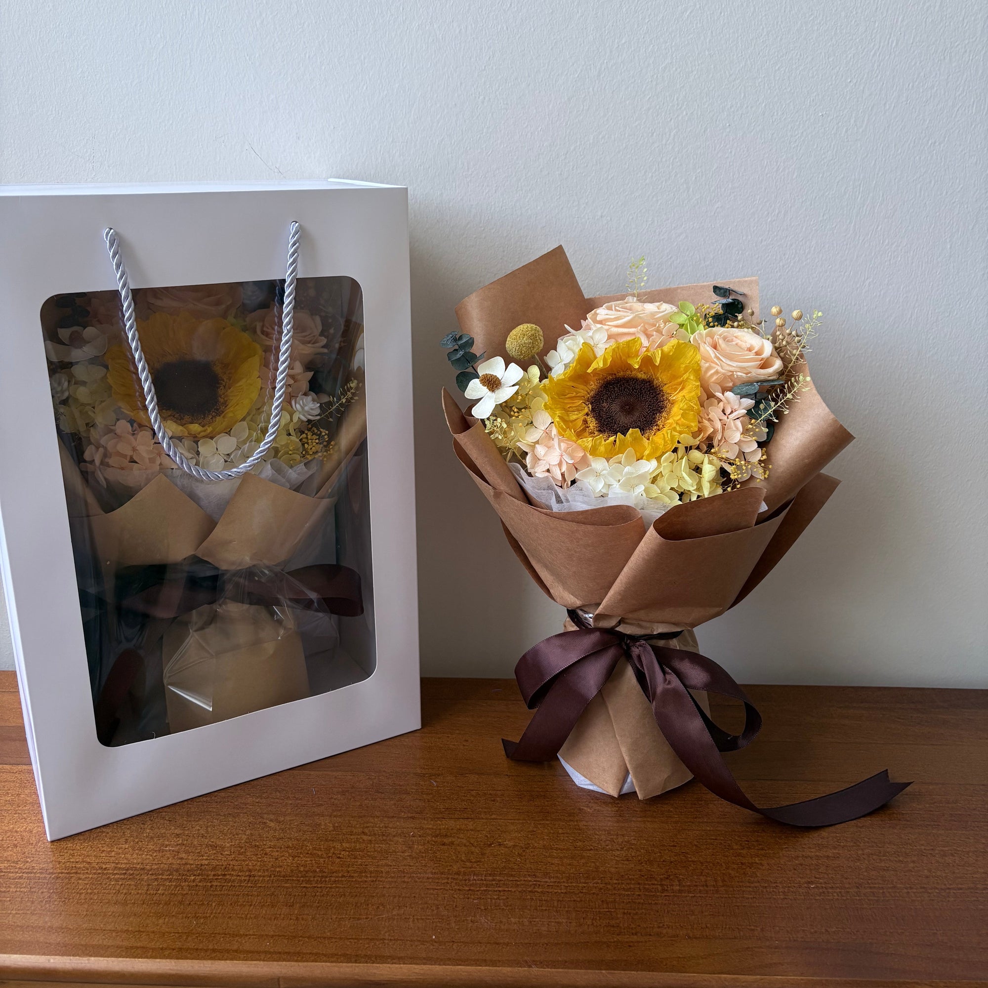 Bouquet of flowers wrapped in brown paper with a bow, placed on a white surface.