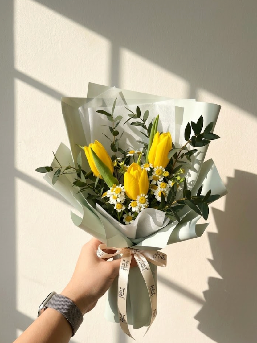 Bouquet of yellow tulips and greenery held by a hand against a light background