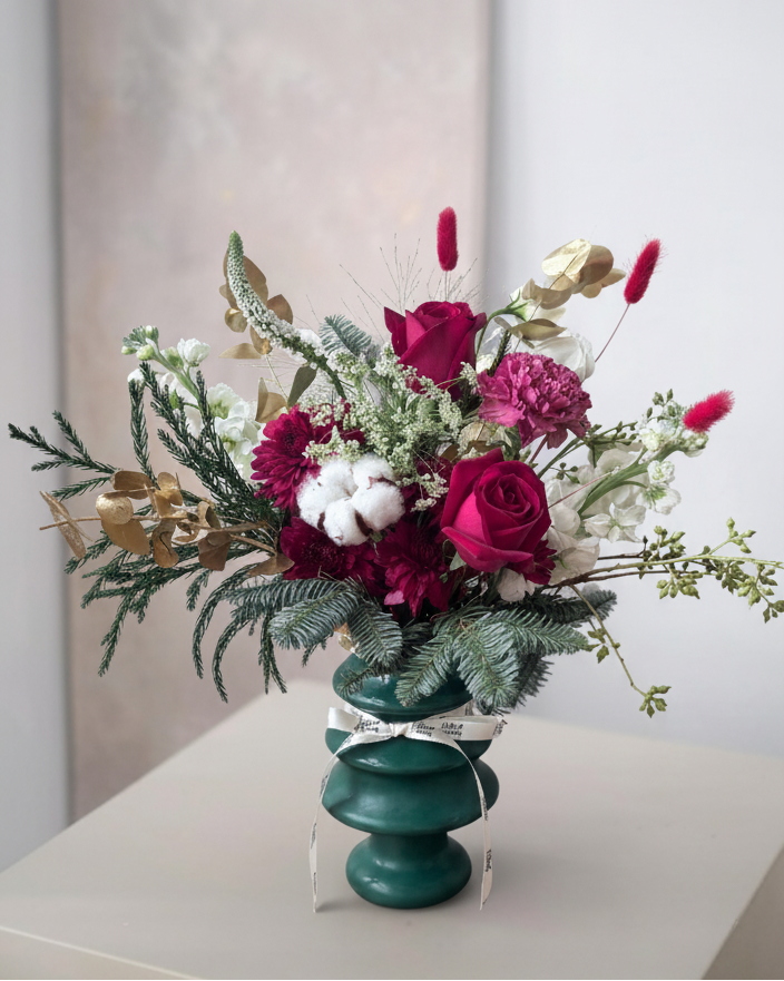 Floral arrangement in a green vase on a white surface with a neutral background
