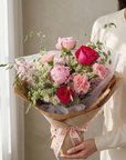 Bouquet of pink and red flowers held by a person against a neutral background